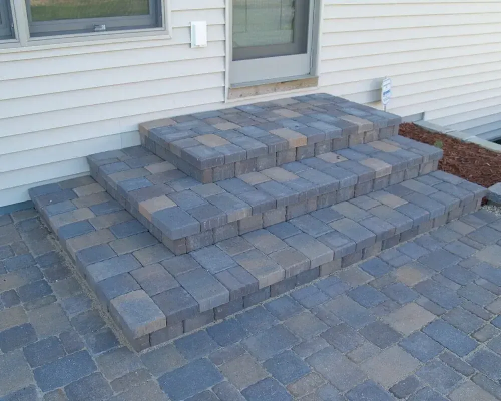 Brick steps leading up to a door, constructed of multicolored pavers, set against a white wall.