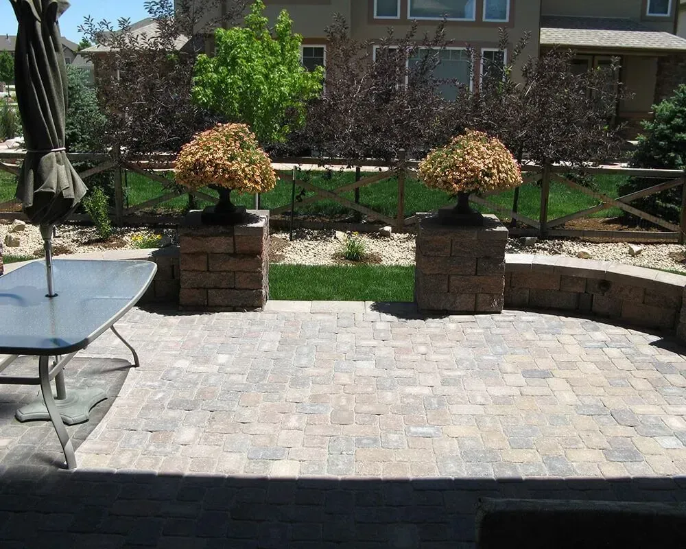 Patio with brick pavers, two potted trees on brick pillars, and a fence.