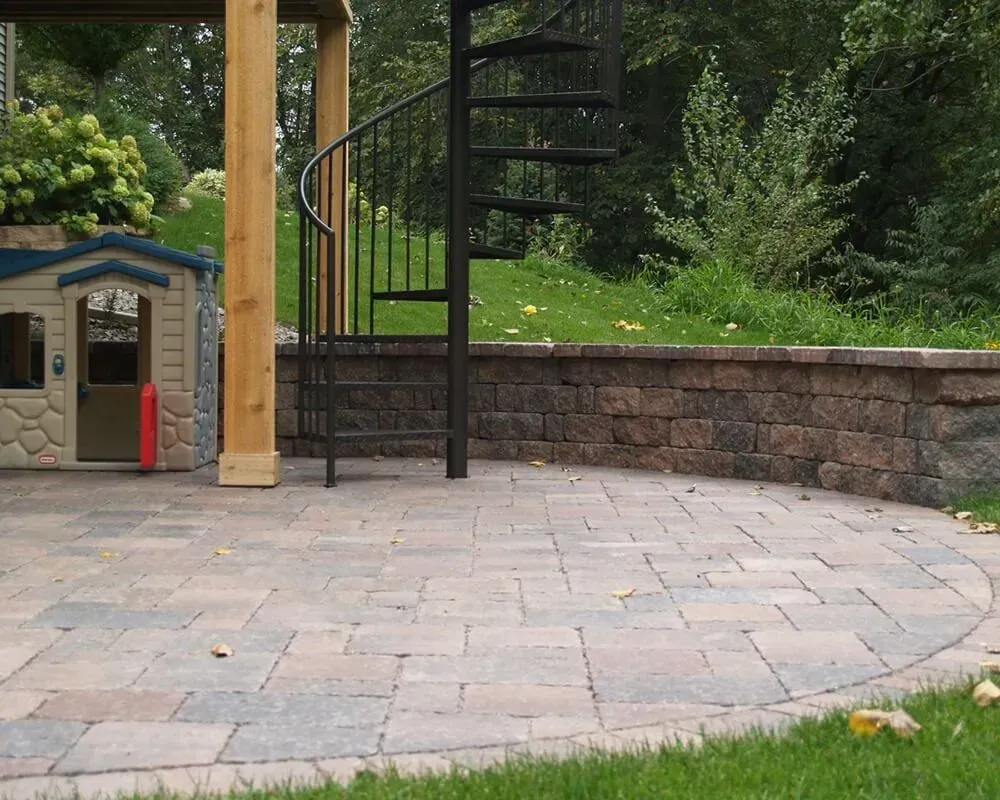 Brick patio with retaining wall, spiral staircase, and children's playhouse in a yard.