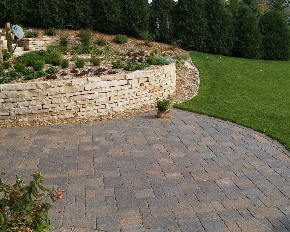 Stone patio with retaining wall, lawn, and landscaping.