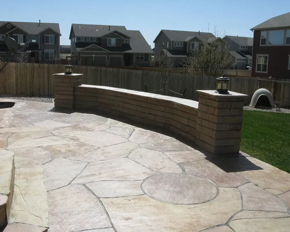 Stone patio with curved brick wall and fence in a residential backyard.