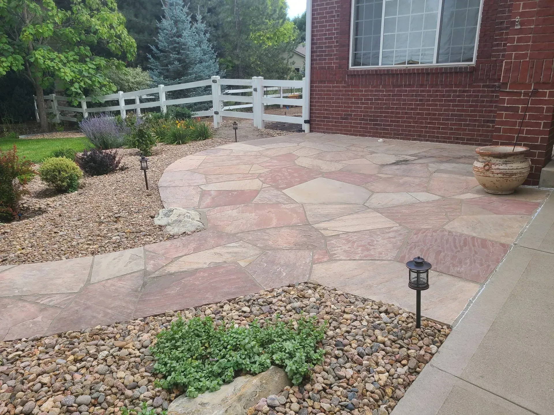 Flagstone patio and walkway edged with river rock, leading to a brick home.