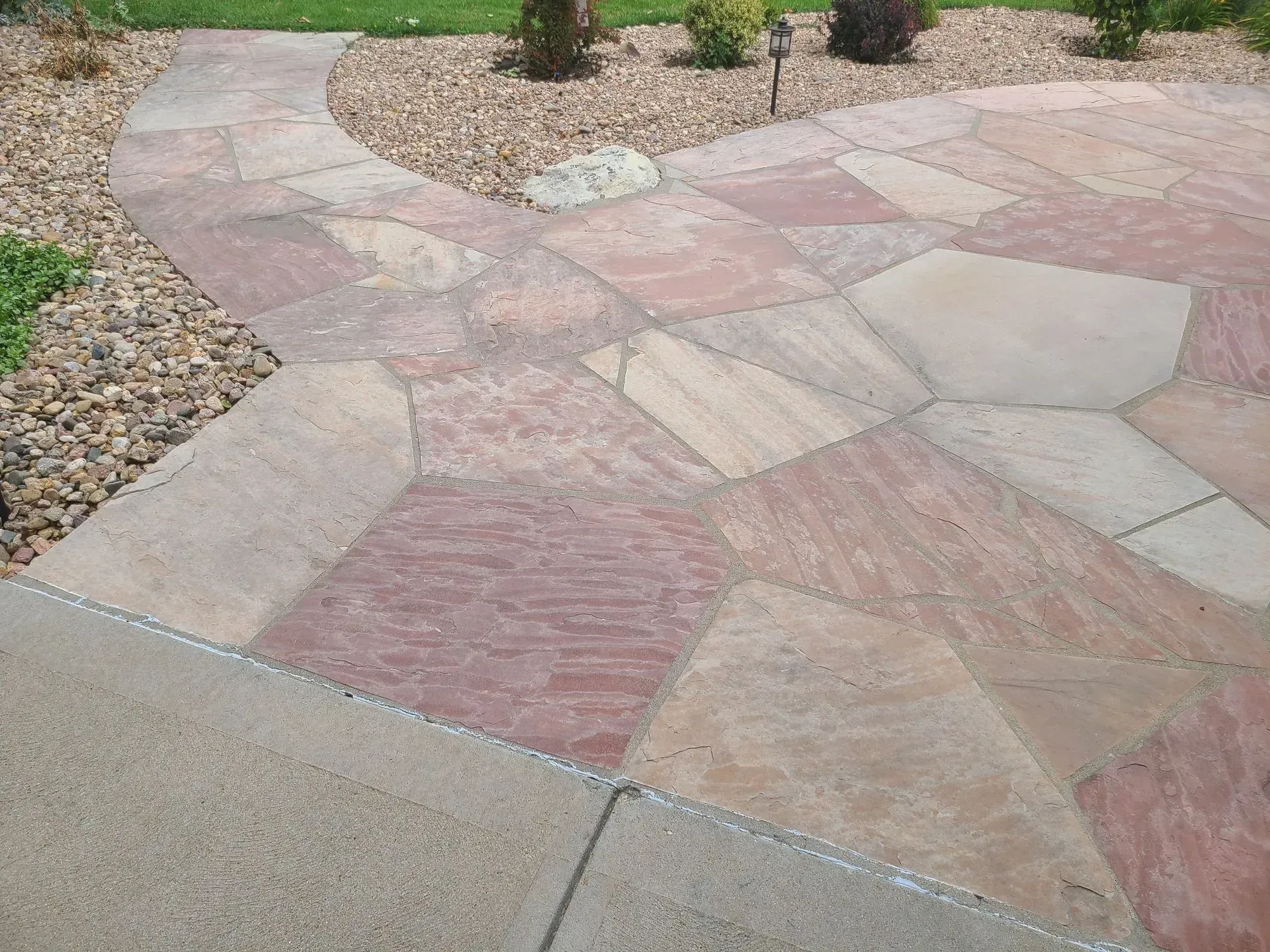 Flagstone patio and walkway with reddish-brown and tan stones, surrounded by gravel and grass.