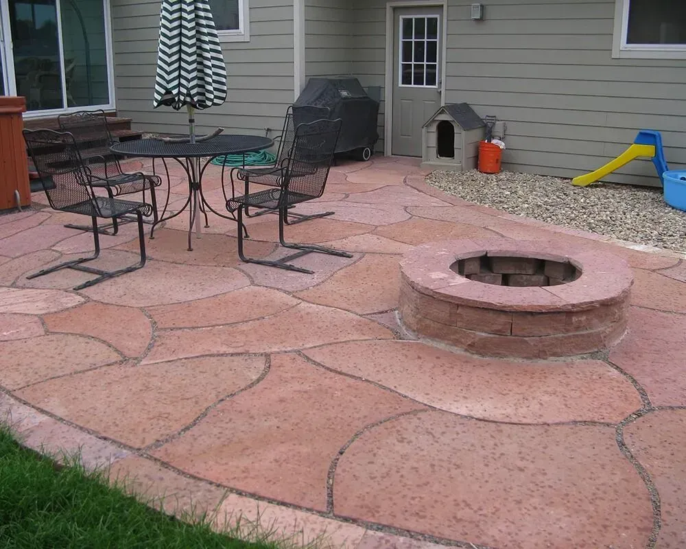 Red flagstone patio with a fire pit, table, chairs, dog house, and a grill.