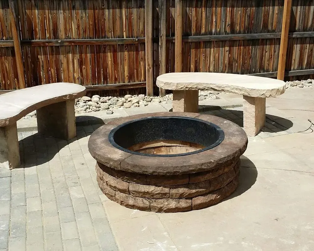 Fire pit with stone benches in a backyard setting; wooden fence in the background.