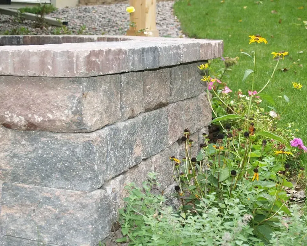 Stone retaining wall with flowers and grass.