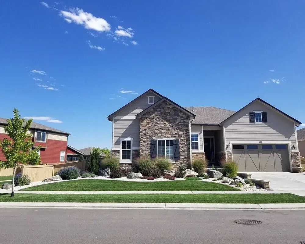 Suburban house with stone accent, blue sky, and green lawn.