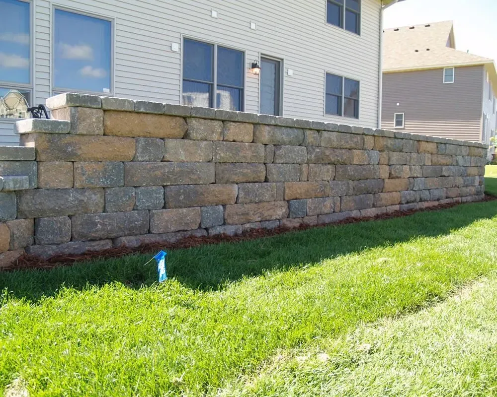 Stone retaining wall next to a house with grass in front.