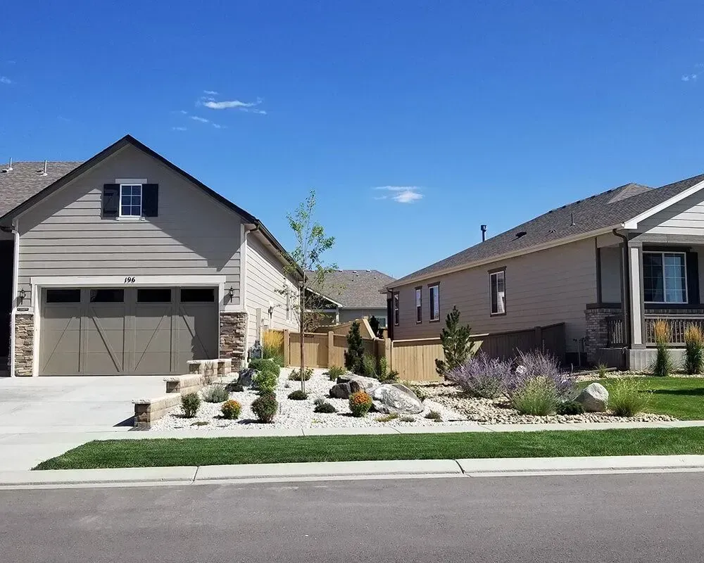 Two homes with landscaping in front, under a blue sky.