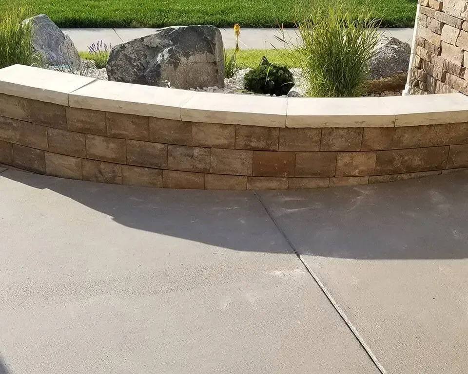 Low brick retaining wall with plants and rocks.