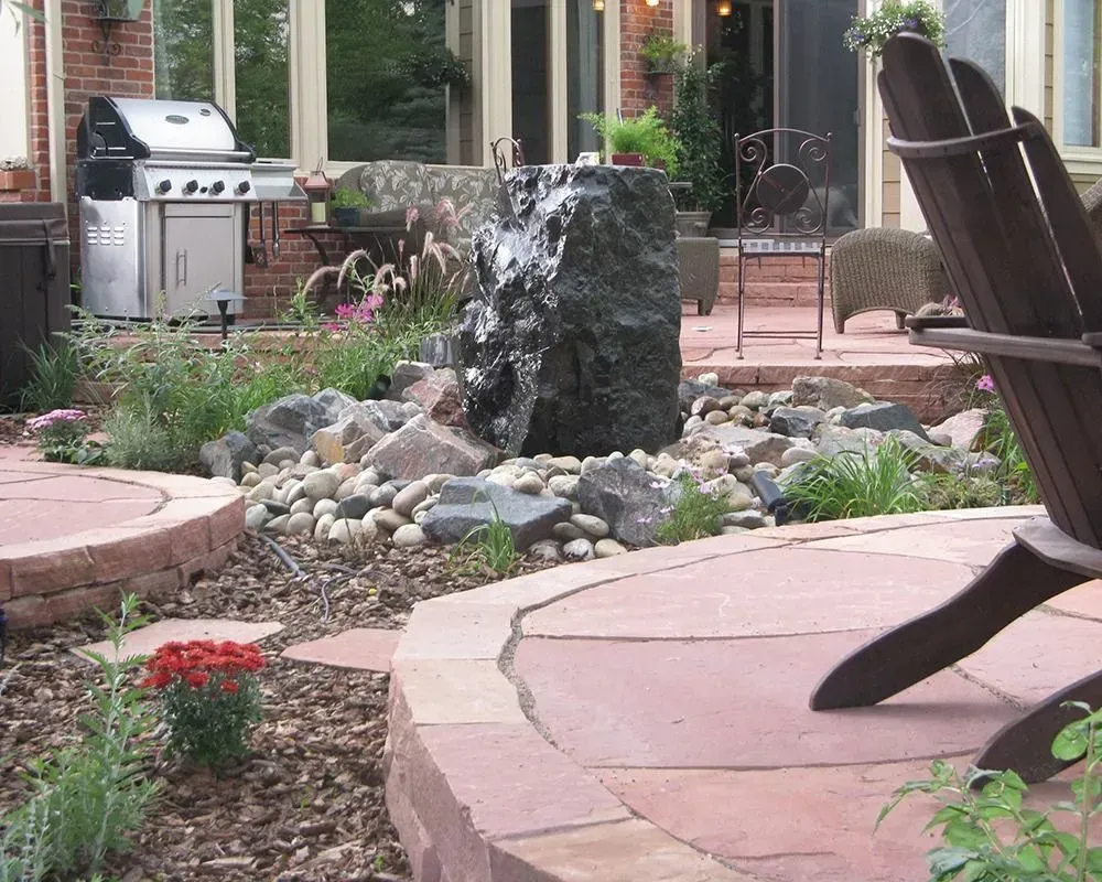 Backyard patio with water fountain, grill, and Adirondack chair.