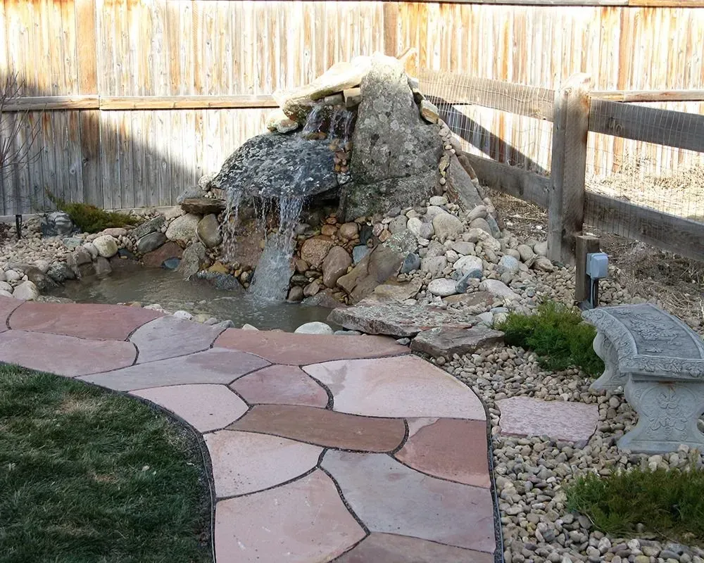 A backyard water feature with a stone waterfall, pond, and stone path.
