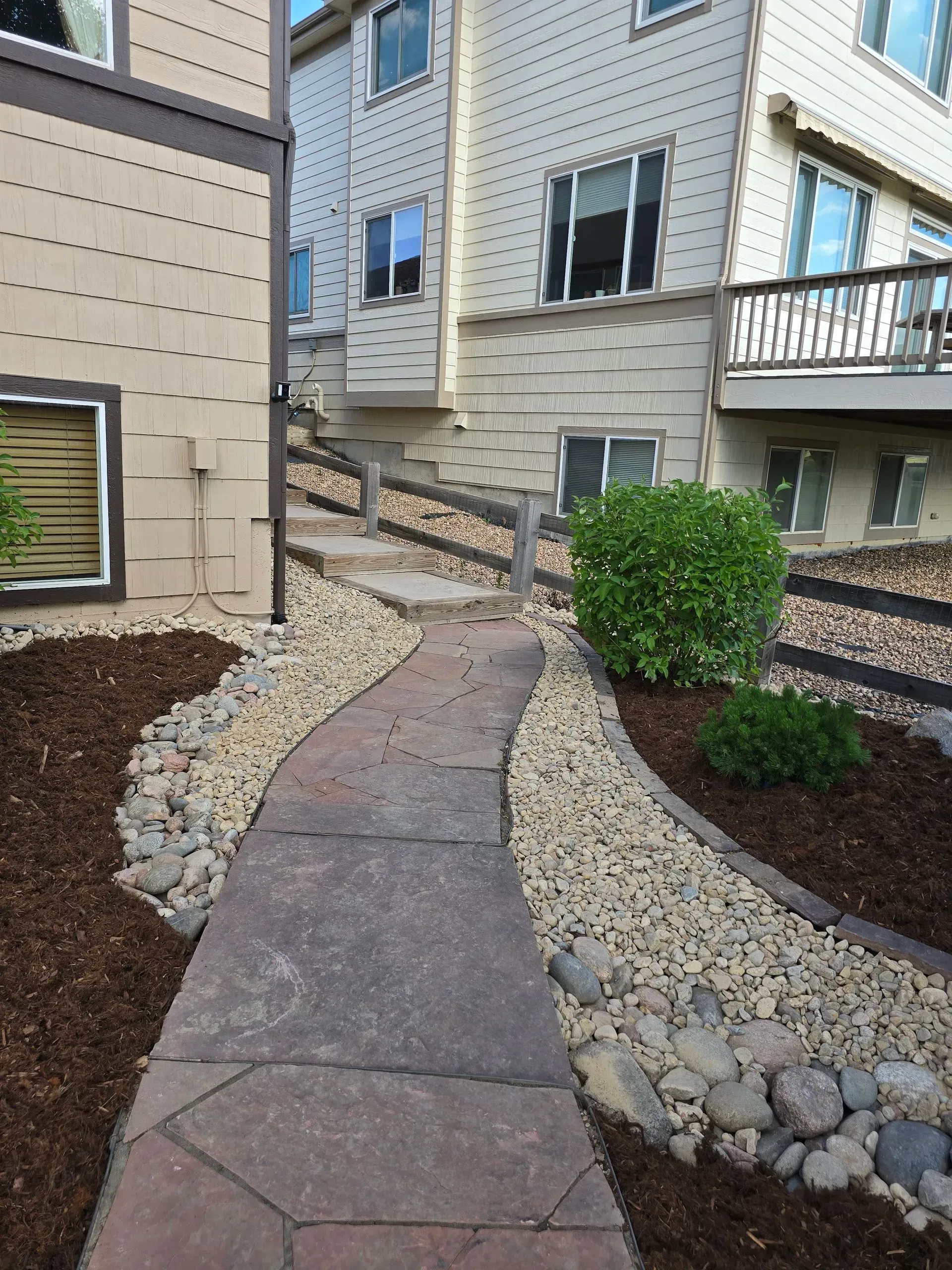 Stone pathway leading uphill between landscaped beds to a multi-story building entrance.