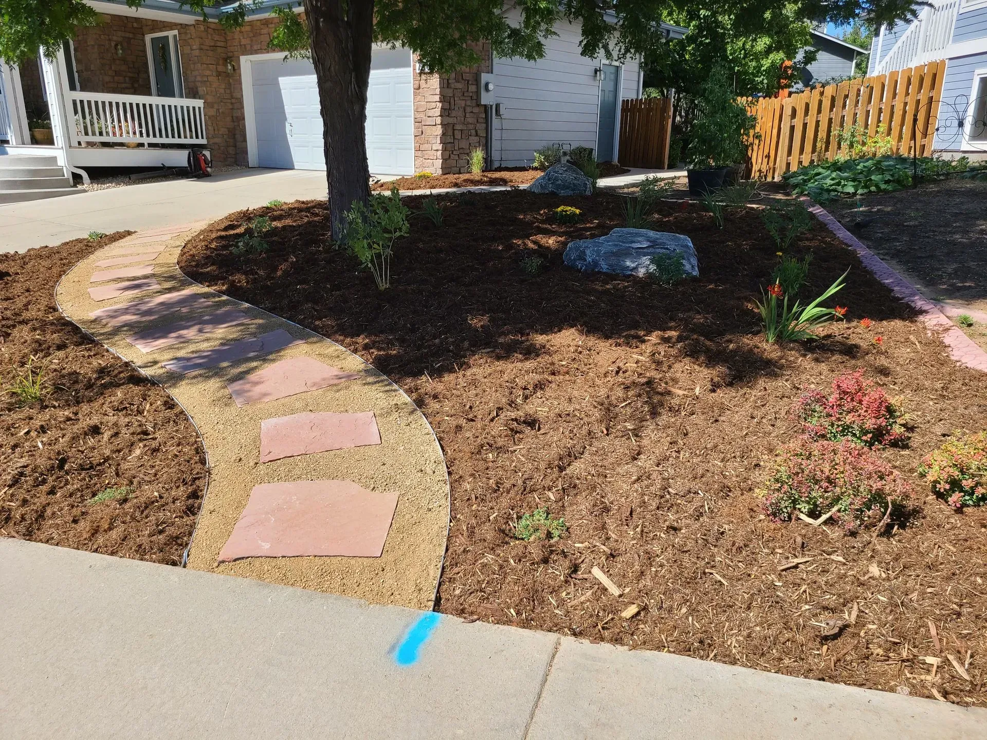 Stone path curves through a mulched front yard with plants, a tree, and a garage.