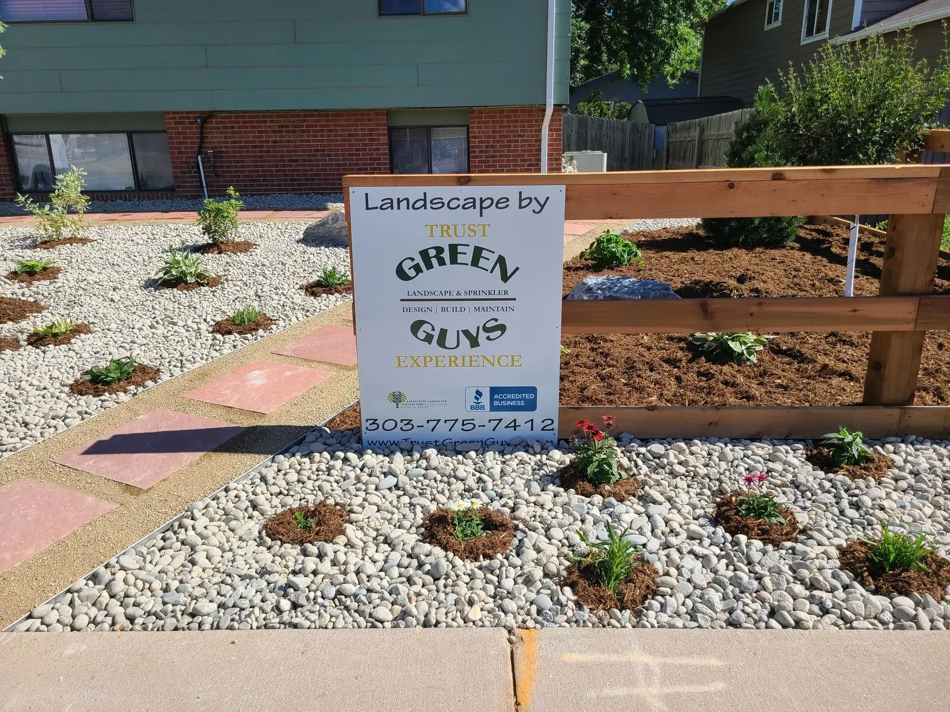 A landscaped yard with small plants and gravel, a sign that reads 