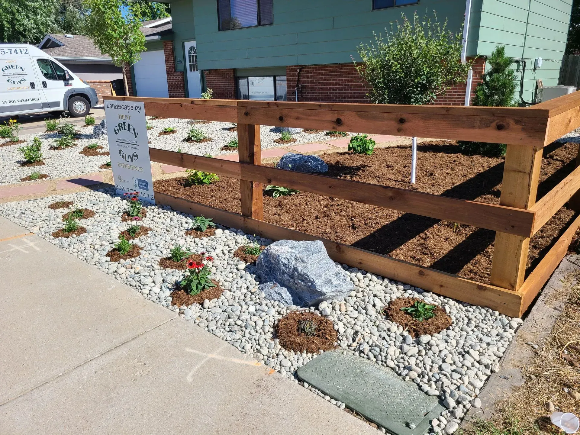 Wooden fence surrounds a xeriscape garden with river rock, mulch, and new plantings.