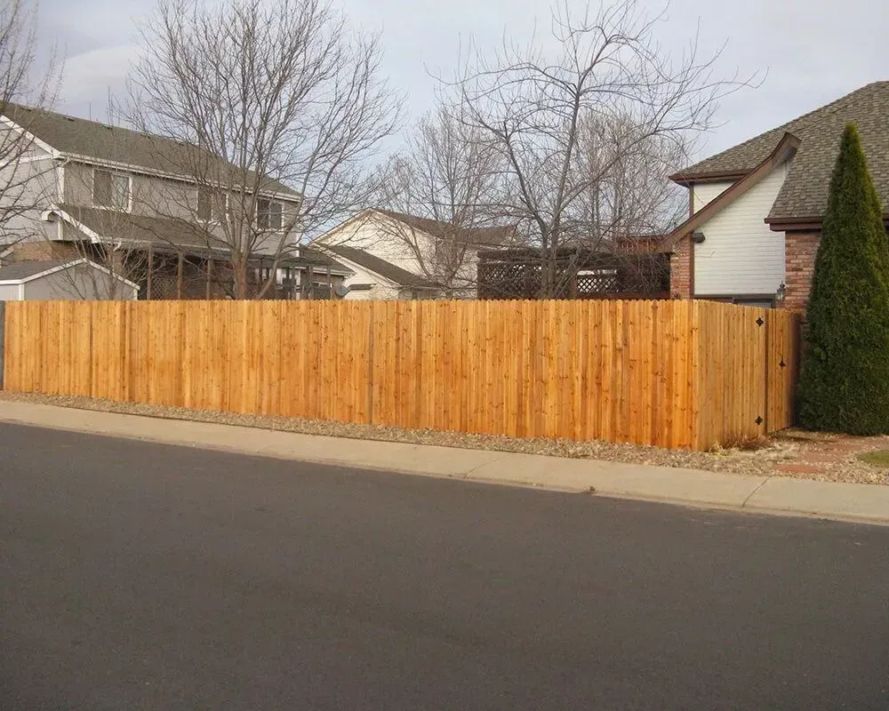 Wooden fence bordering a residential street with homes in the background.