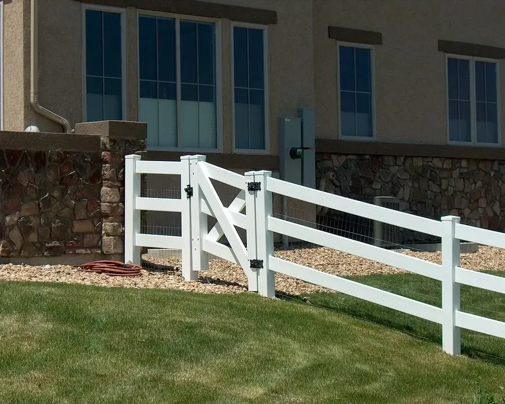 White vinyl fence and gate in front of a house with stone accents and windows.