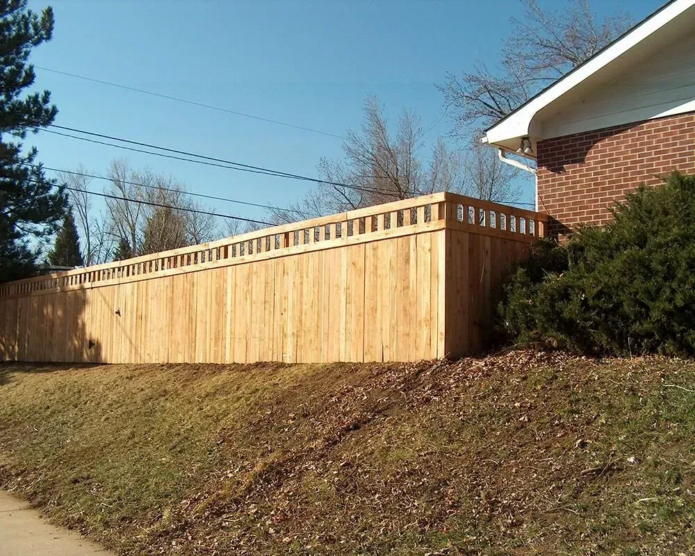 Wooden fence bordering a yard next to a brick house on a sunny day.