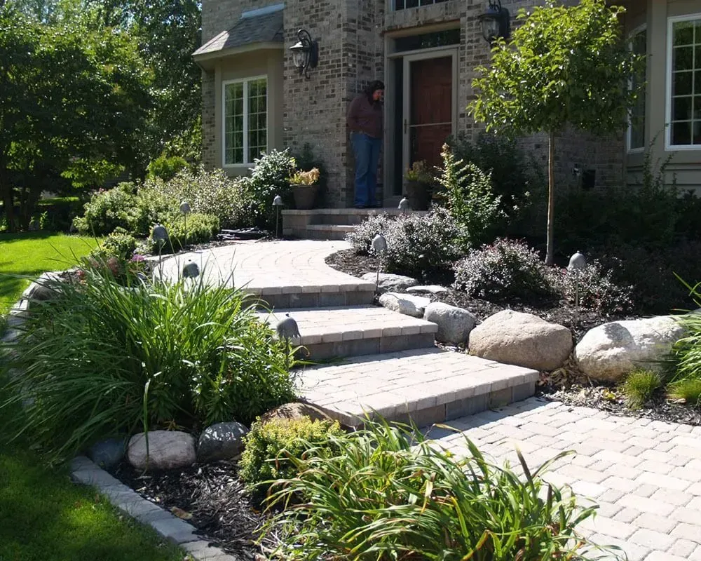 Stone walkway and steps leading to a brick home's front door, flanked by landscaping and greenery.