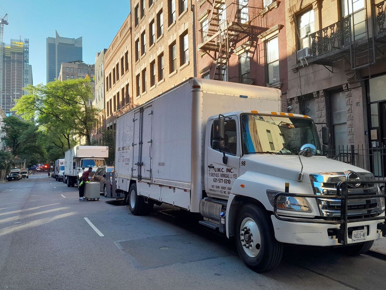 White box truck parked on a city street beside brick buildings and sidewalk scaffolding.