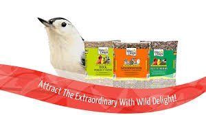 A bird is sitting next to three bags of bird food.