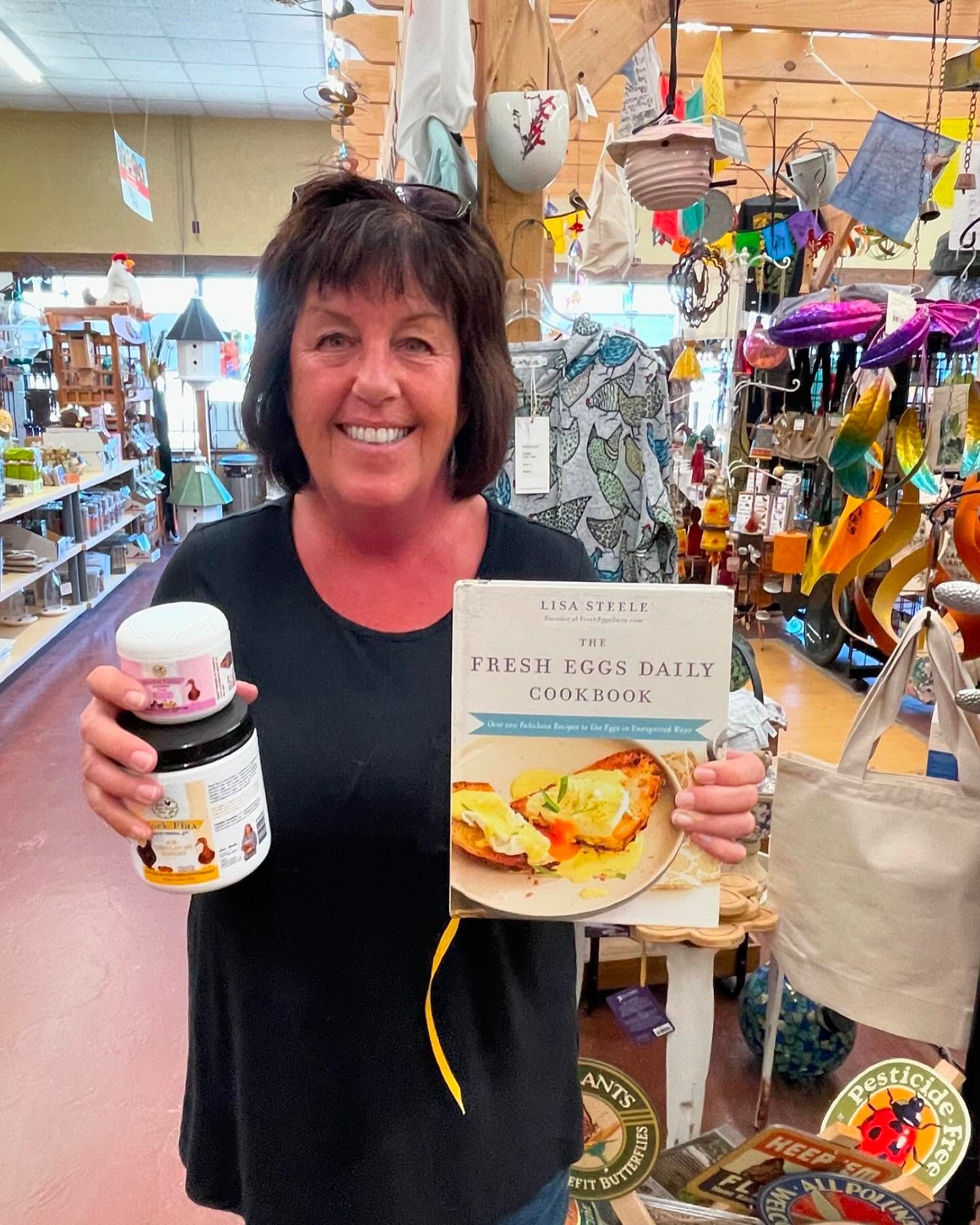A woman is holding a cookbook and a jar of jam in a store.