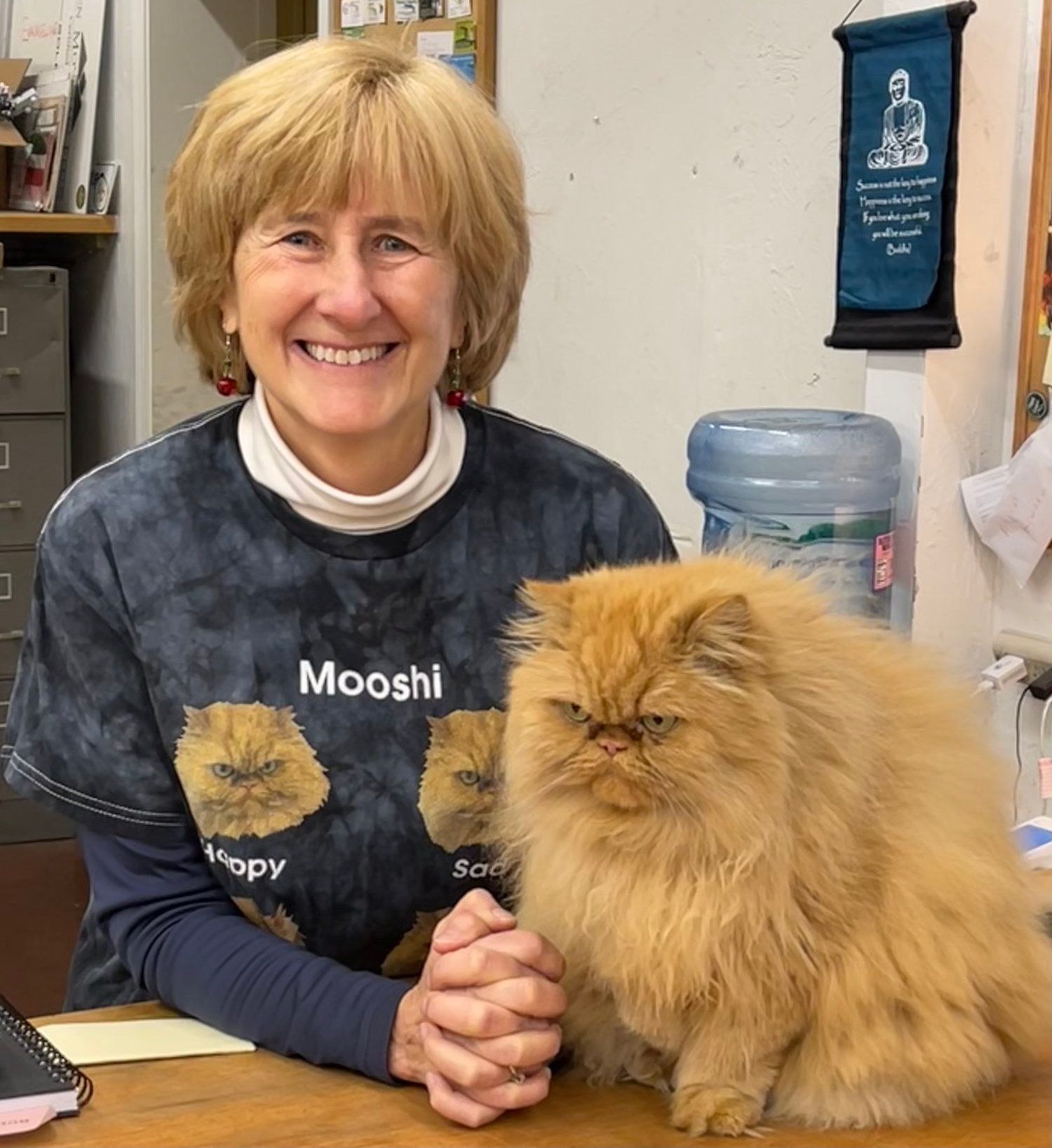 A woman wearing a mooshi t-shirt sits next to a fluffy cat