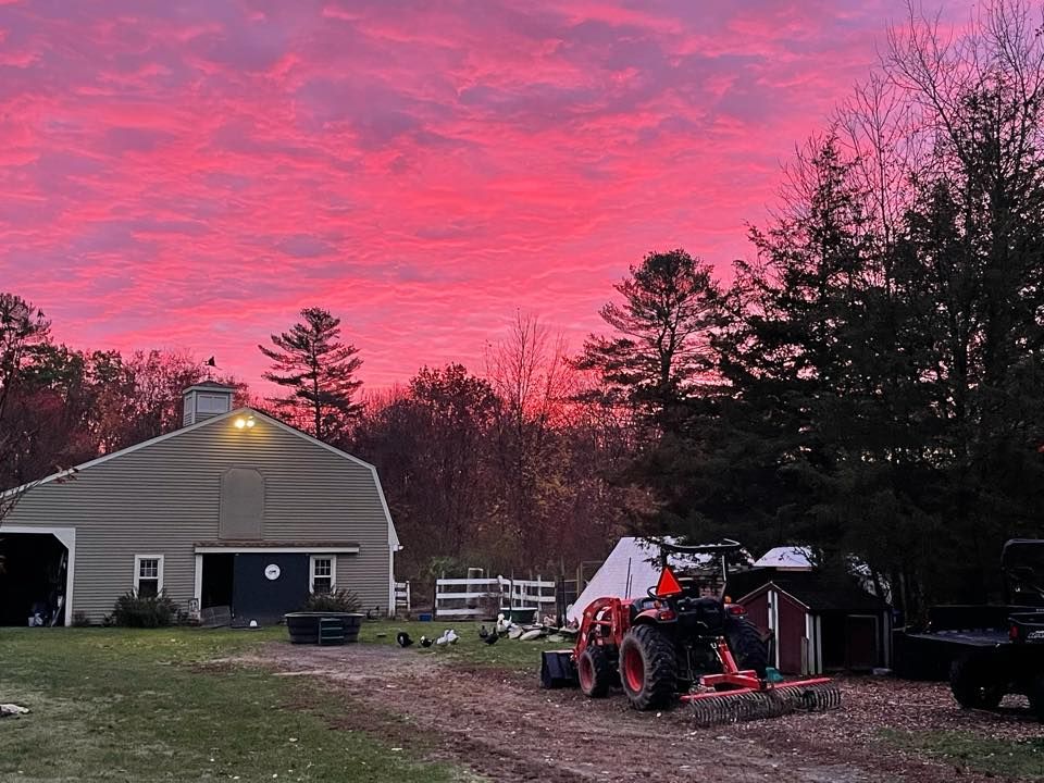 A tractor is parked in front of a barn at sunset.