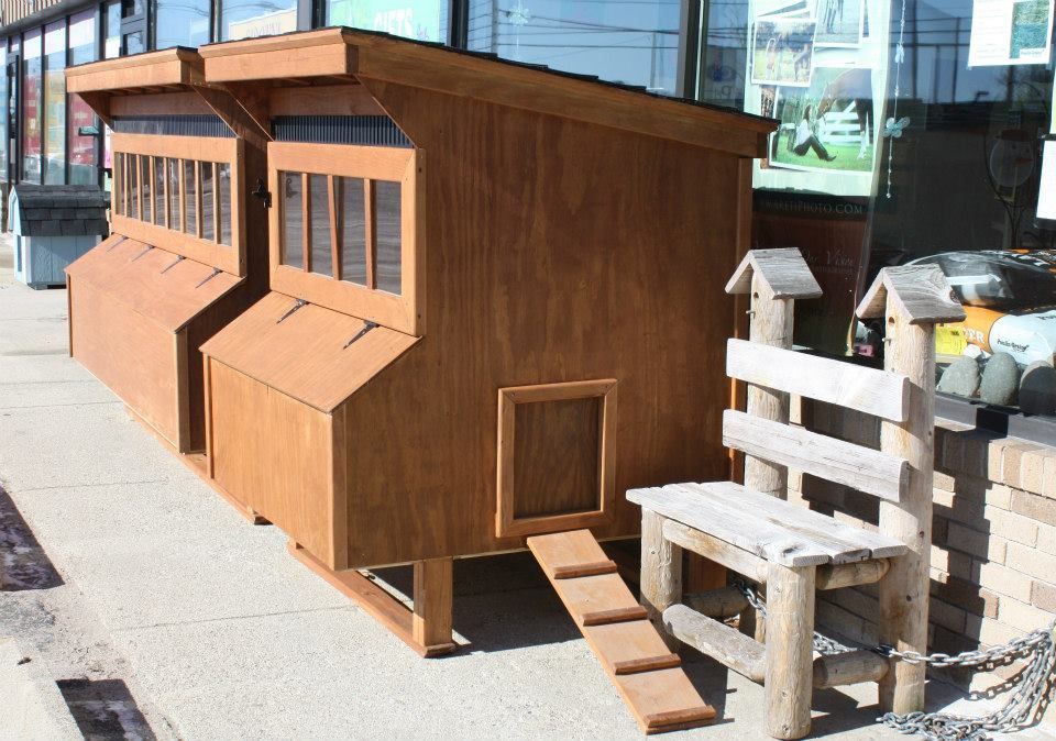 A wooden chicken coop is sitting on the sidewalk next to a wooden bench