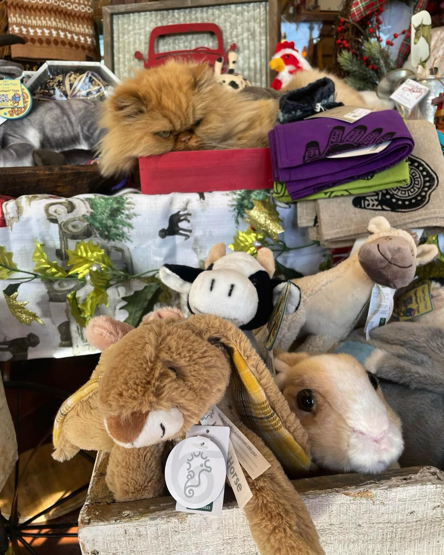 A cat is sleeping on top of a pile of stuffed animals.