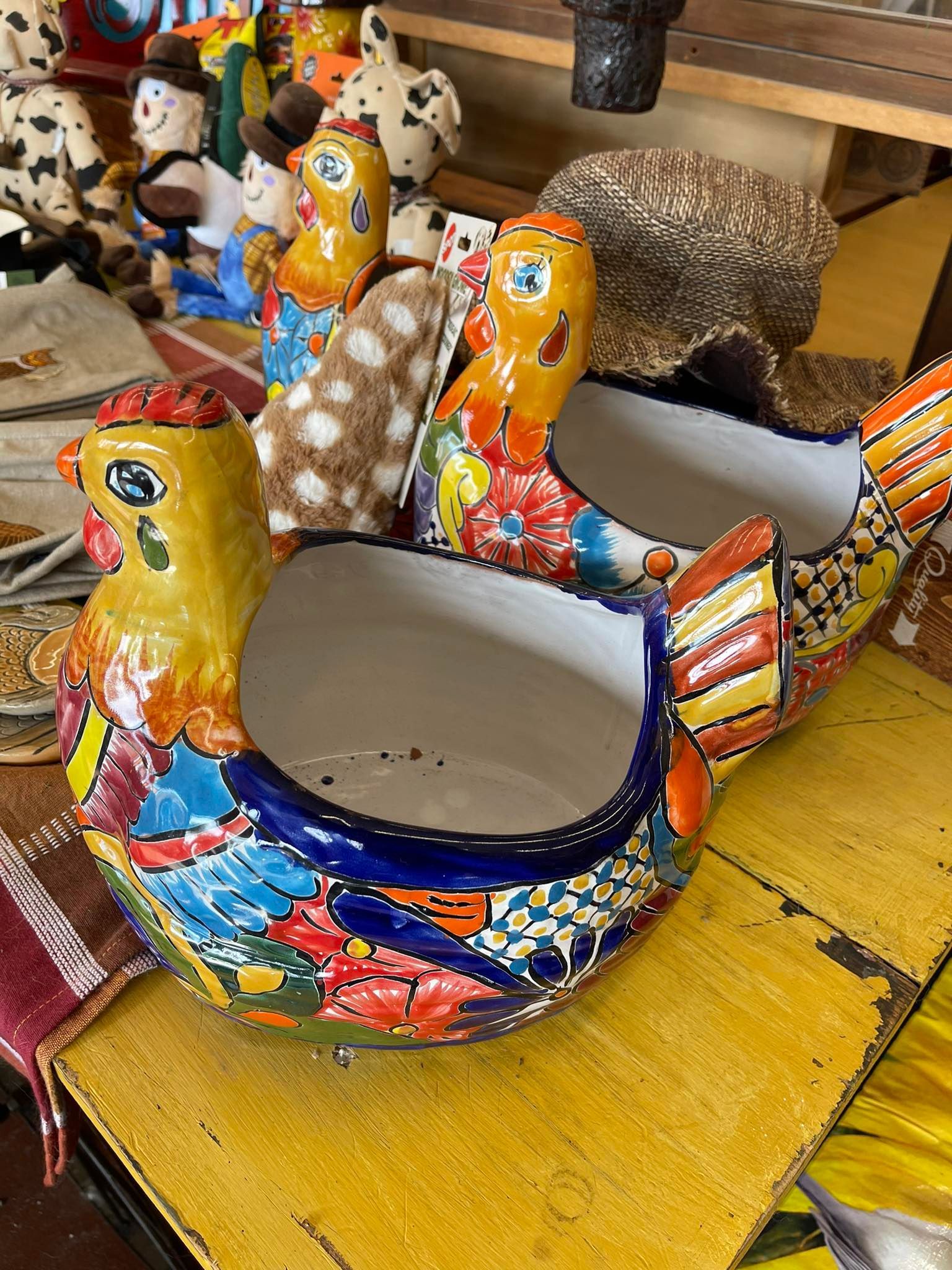 Two colorful ceramic chickens are sitting on a yellow table.