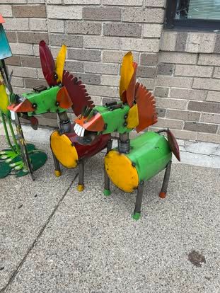 Two colorful metal animals are sitting on the sidewalk in front of a brick building.