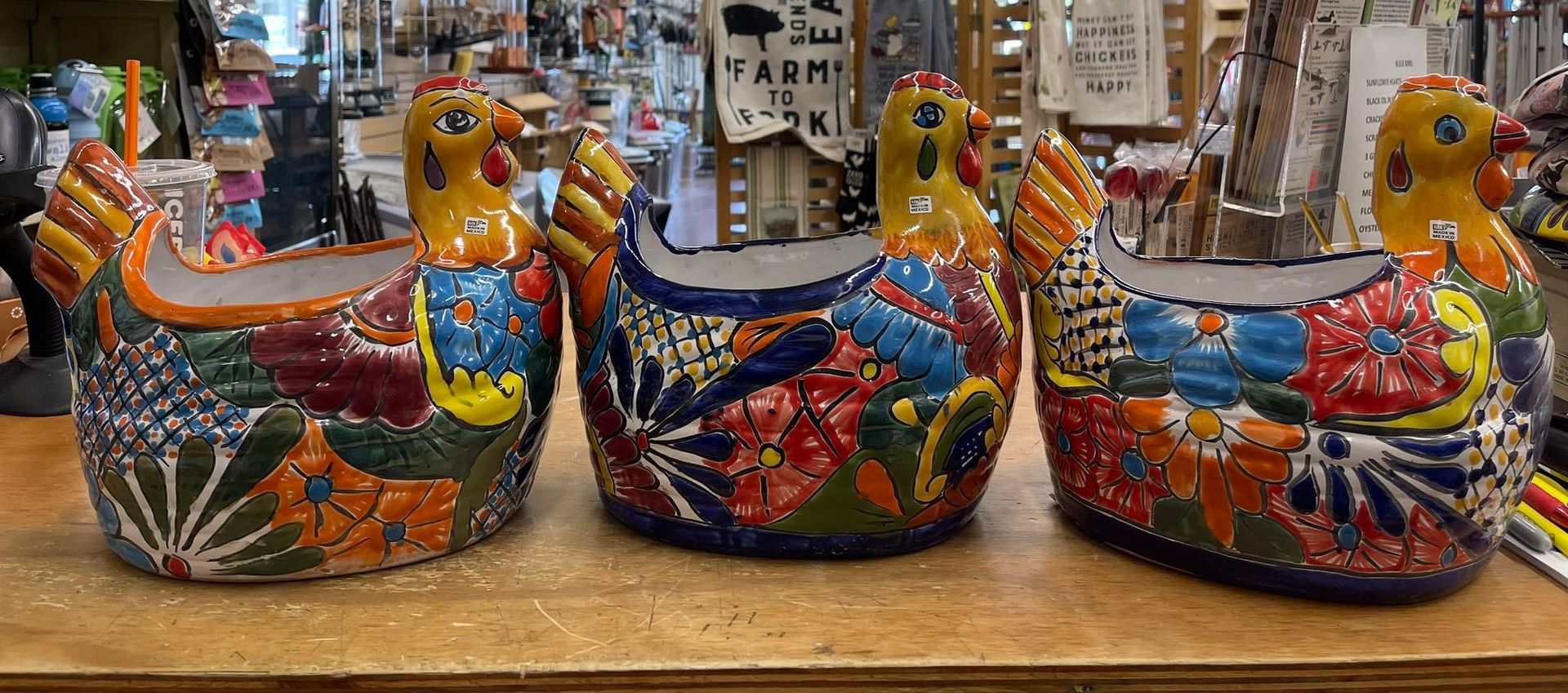 Three colorful ceramic chickens are sitting on a wooden table.
