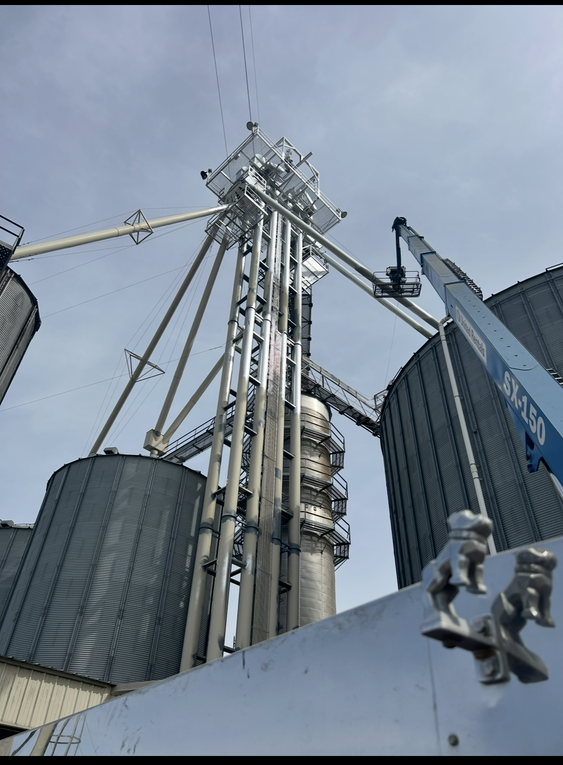 Grain elevator facility with tall structures and silos against a light blue sky.