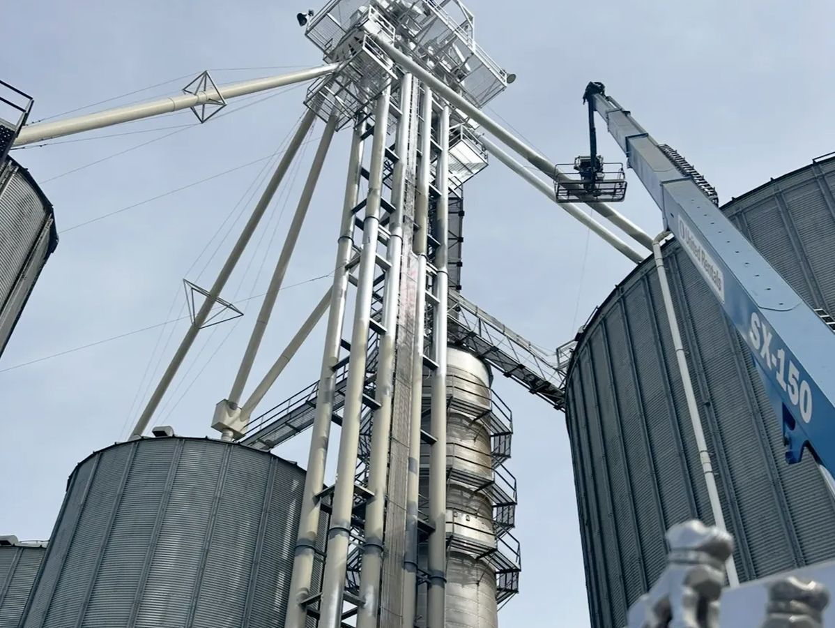 Grain silos and elevator tower against a cloudy sky, with a blue lift in the corner