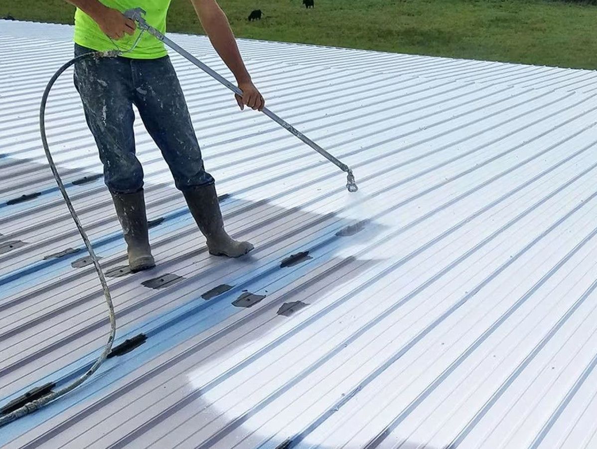 Person spraying a white coating on a corrugated metal roof