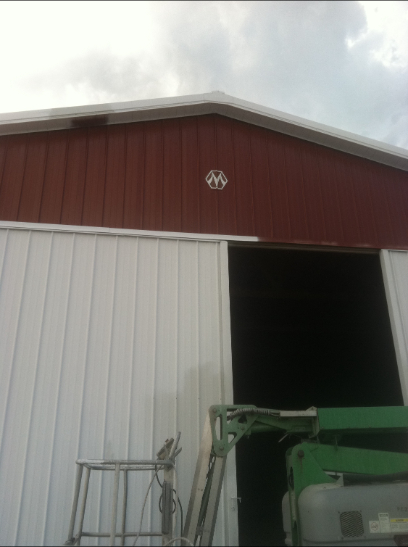 Red and white barn with a large door opening and logo above. A lift is parked in front of the door.