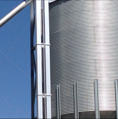Galvanized metal grain silo and support structure against a clear blue sky.