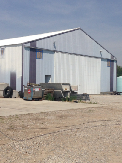 Large metal building with white and blue panels, concrete pad, and debris in front.