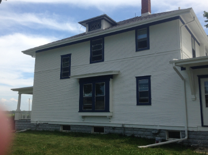 White two-story house with dark blue trim, a small front porch, and dormer under a blue sky.