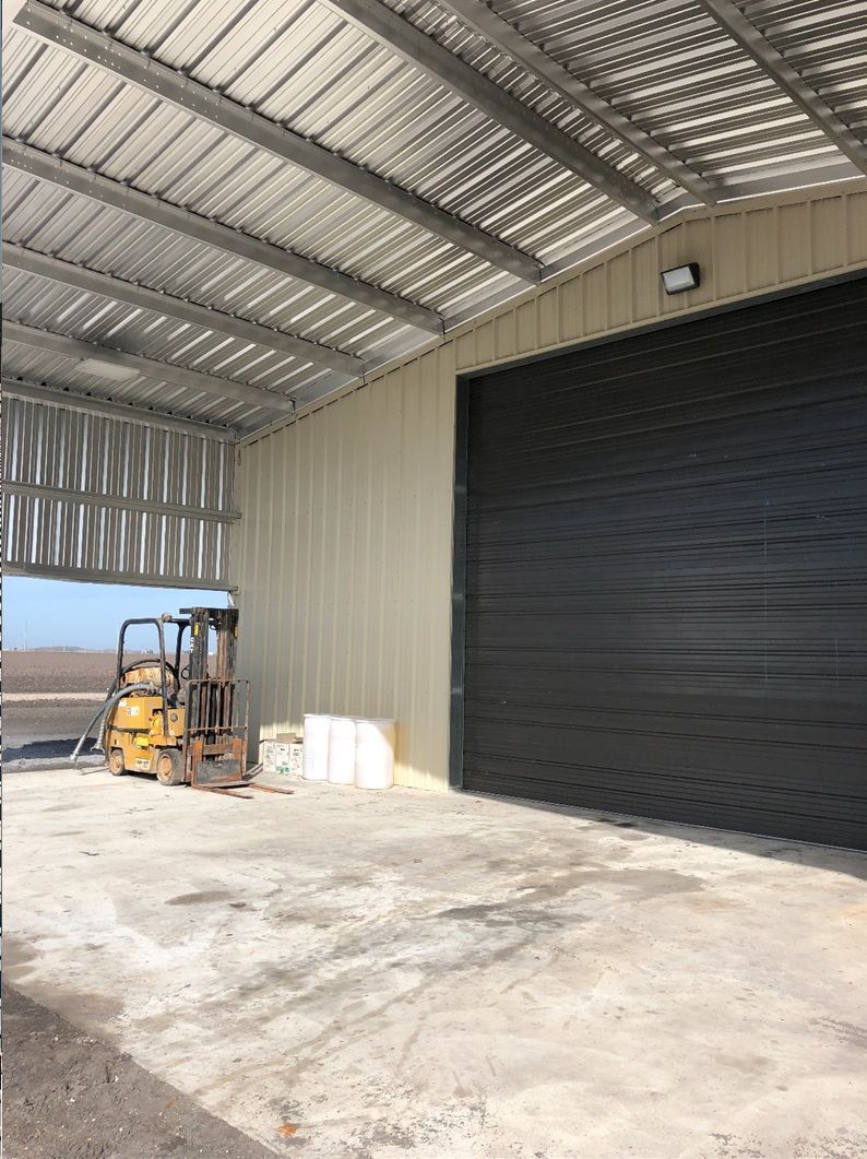 Open warehouse with a closed black garage door, forklift, and metal roof.