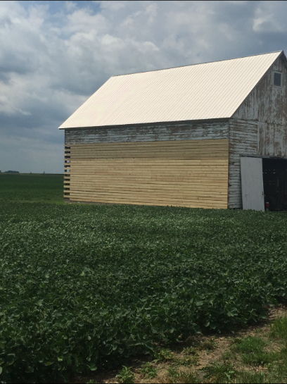 Weathered barn with new wooden siding in a green field under cloudy sky.