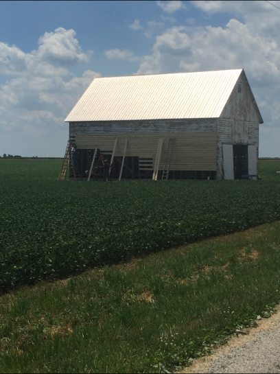 White barn with metal roof in a green field under a cloudy sky.