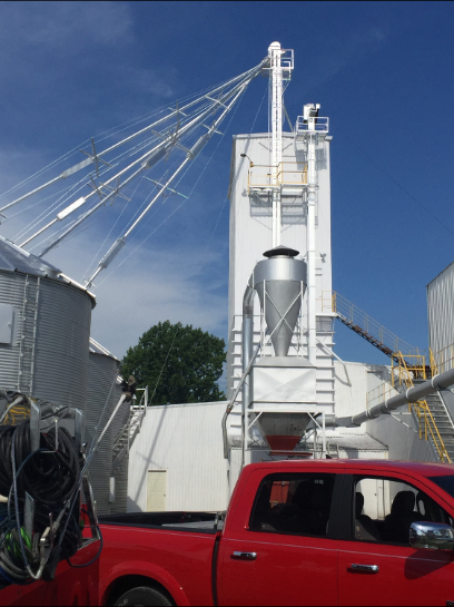 Red truck parked near grain silo and white industrial processing tower against a blue sky.