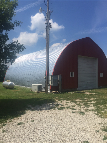 Red barn with corrugated metal roof and white garage door under a blue sky.