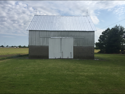 Barn with silver roof and white doors, set in a grassy field under a cloudy sky.