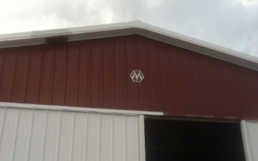 Red and white barn exterior with large open doorway and a logo near the roof.