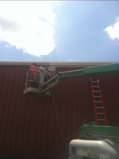 Worker in cherry picker repairing building siding under a blue sky.