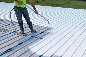 Person spraying a white coating on a corrugated metal roof.
